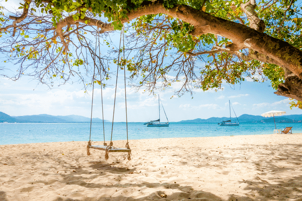 rang yai beach with a swingset in the foreground and sailing ships anchored in the waters