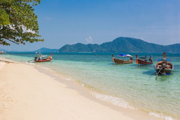 long tail boats approaching the shores at rawai beach full of tourists